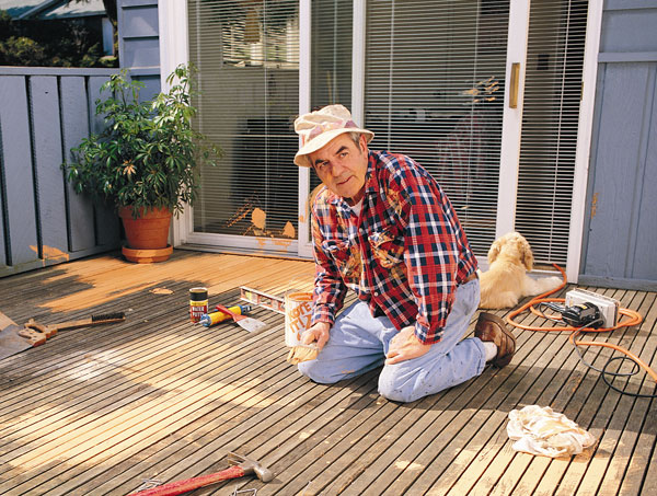 Spring deck maintenance checklist - Homeowner laboring on refinishing wood deck